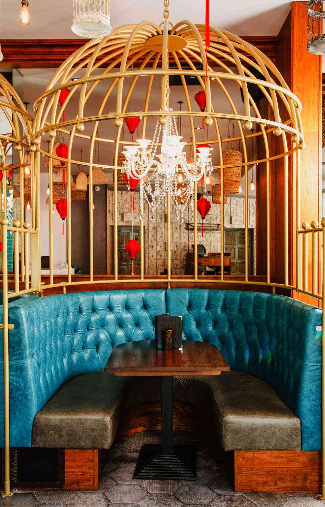 A gold birdcage booth with teal leather seating and a chandelier at Siamais