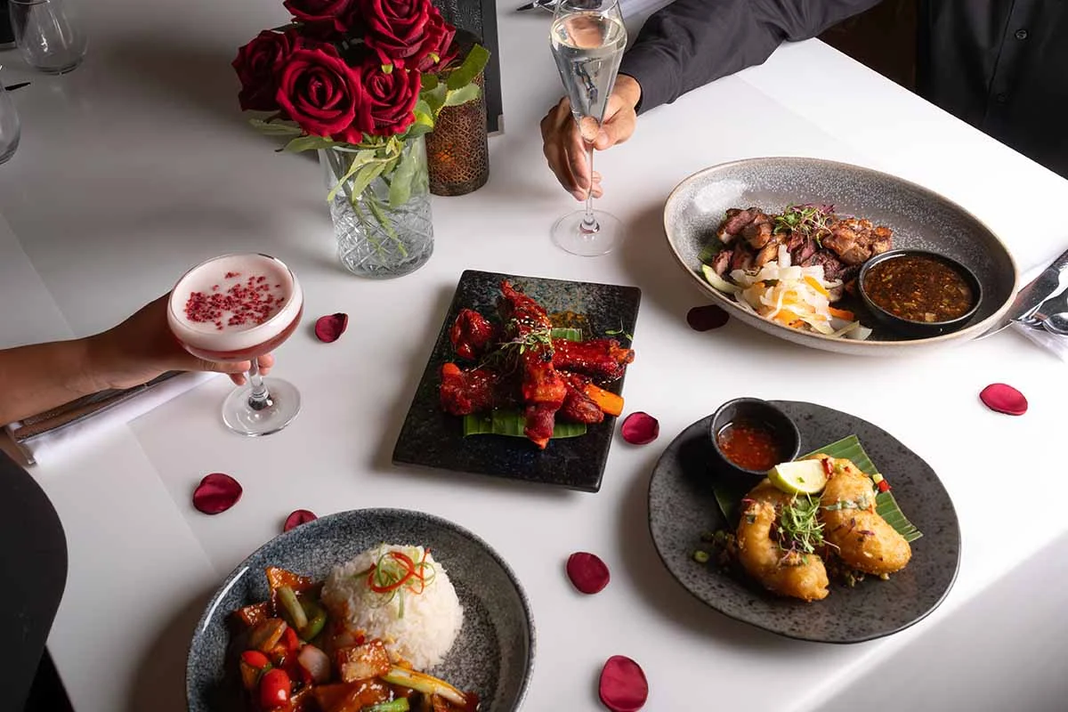 Guests sharing Thai dishes and cocktails at a white-clothed table