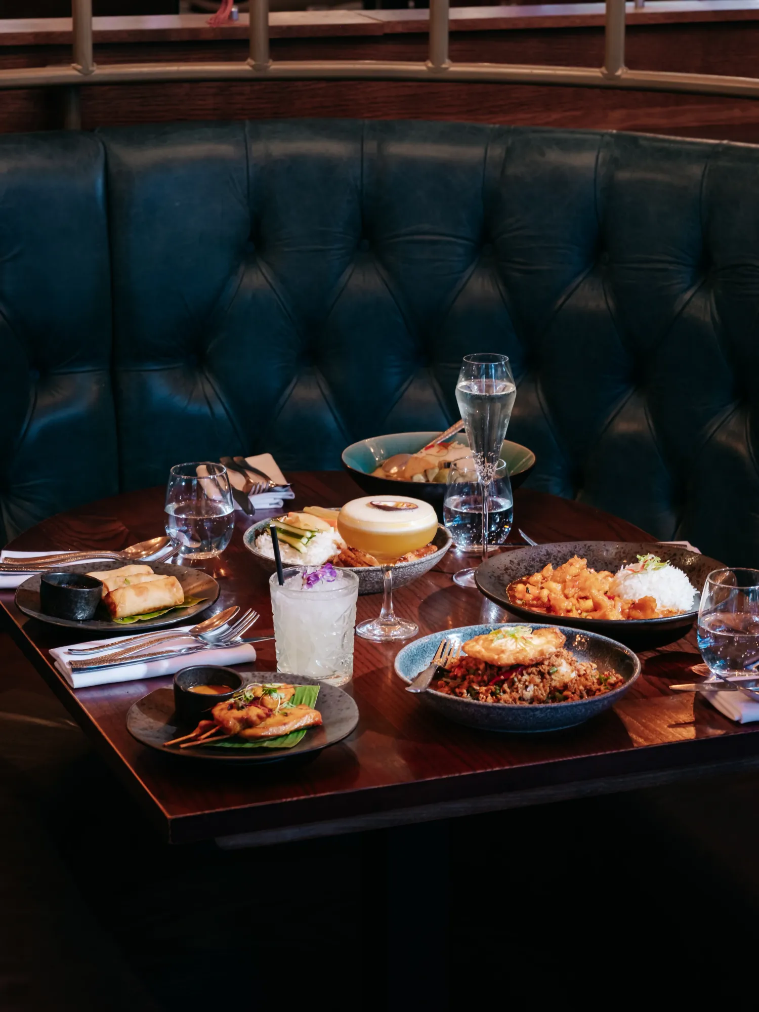 Bottomless brunch dishes and cocktails laid out in a teal booth at Siamais